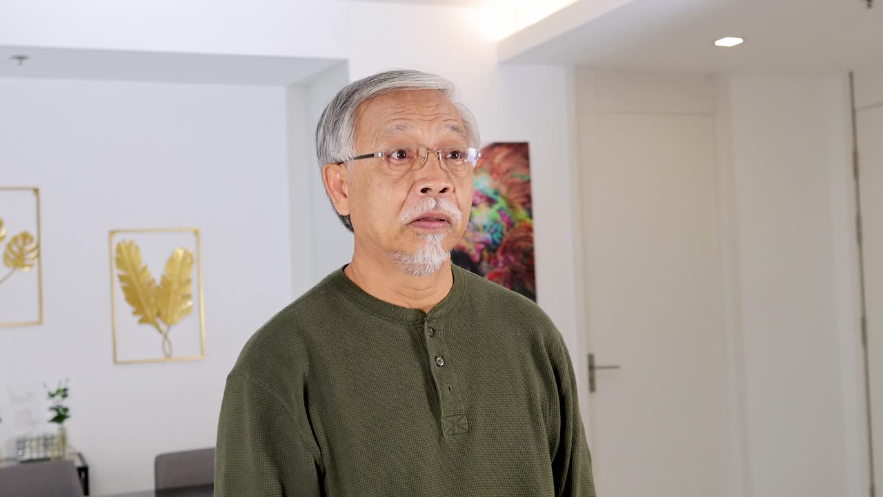 Senior man signals quiet with finger to lips, standing in bright, contemporary indoor setting