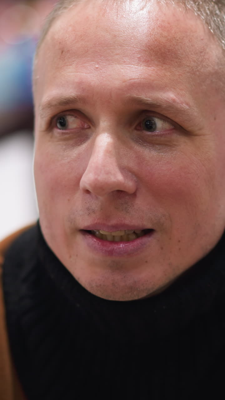 primer plano de un hombre calvo de mediana edad riendo de corazón, vestido con un suéter marrón y una bufanda negra, con un fondo borroso de personas patinando sobre hielo