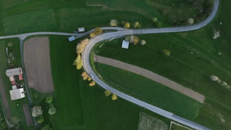 Drohnenansicht-Von-Oben:-Vorfrühling-Und-Ein-Einsames-Auto-Fährt-Eine-Kurvenreiche-Hügelstraße-Hinauf,-Während-Die-Sonne-Untergeht-Und-Einen-Warmen-Schein-Auf-üppiges-Grünes-Gras-Wirft