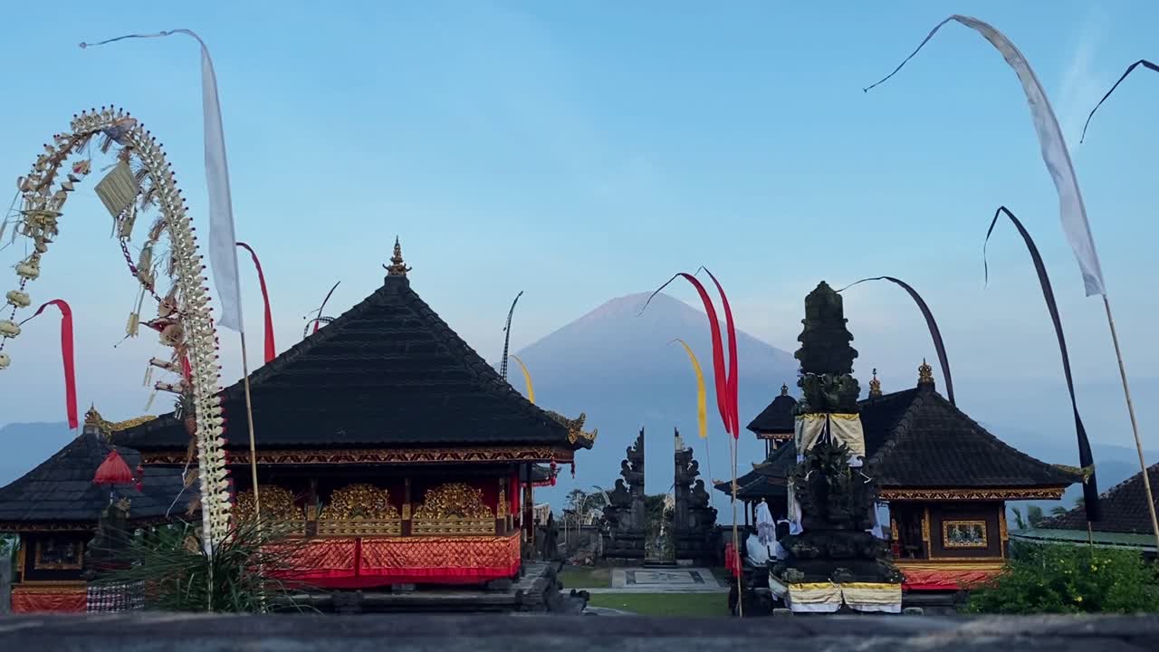 Little temple houses with flags hanging and blowing in wind with volcanic landscape in background, unique Balinese architecture set amidst natural scenery