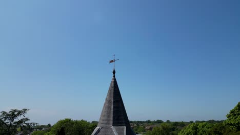 Drone-crane-shot-of-a-village-church-wooden-steeple-with-blue-skies-behind-it