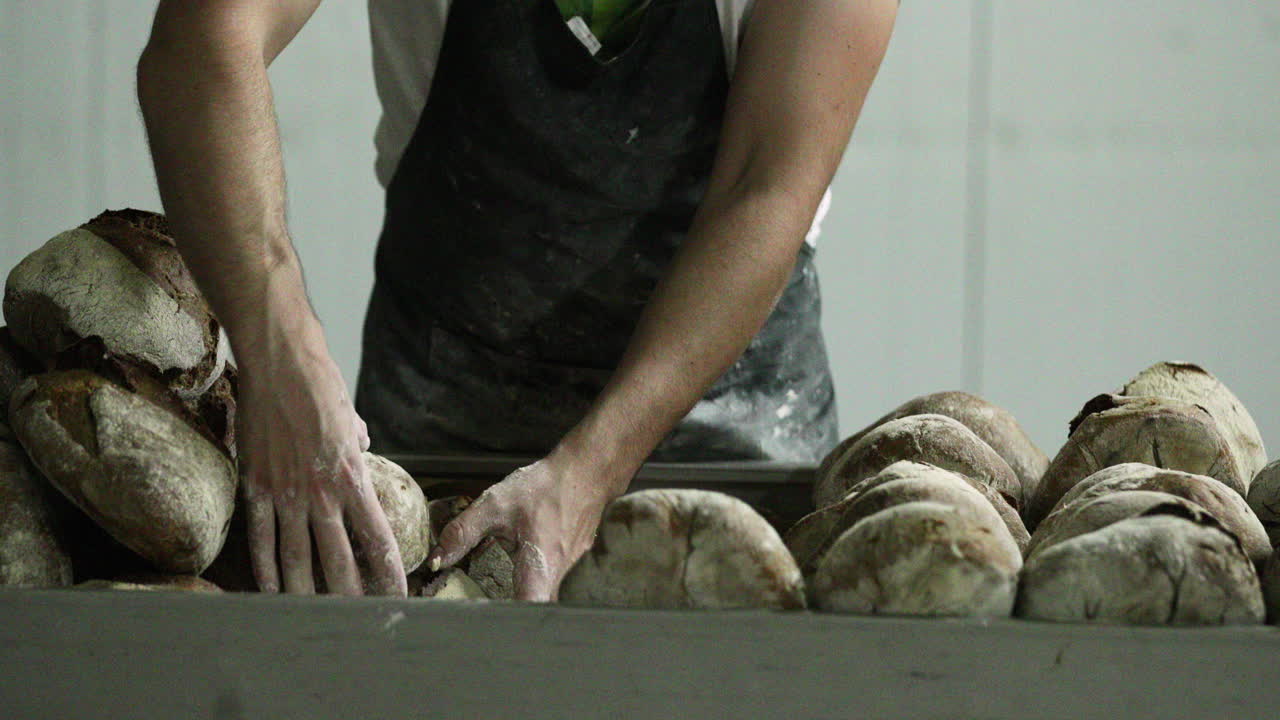 Baker Arranging Freshly Baked Bread In Neat Piles - medium shot