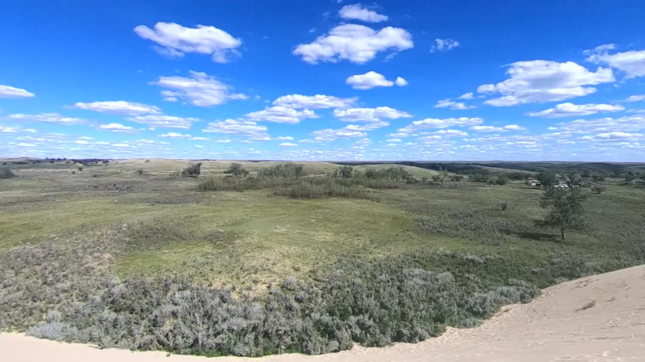 Standing on a mountain on sand looking down at the prairies in the country near Alberta Canada on a sunny day with clouds in the sky and sun wind blowing around the grass and trees