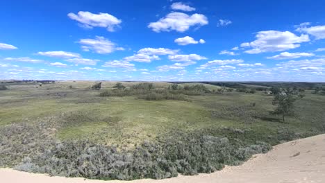 standing on a mountain on sand looking down at the prairies in the country near alberta canada on a sunny day with clouds in the sky and sun wind blowing around the grass and trees