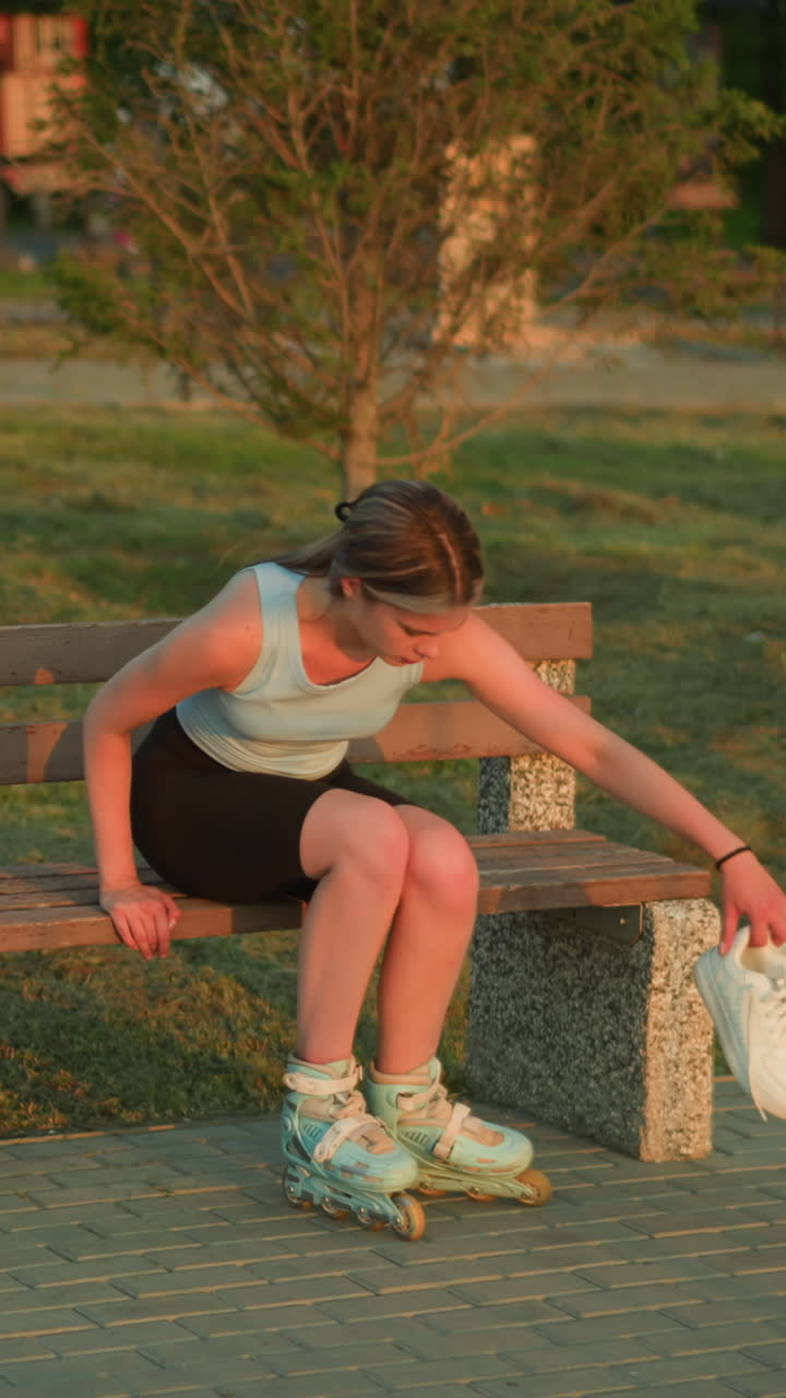 joven sentada en un banco al aire libre dejando caer zapatillas blancas de su mano mientras usa patines, rodeada de vegetación, árboles y elementos arquitectónicos en el fondo