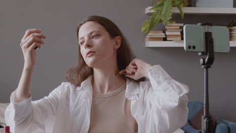 joven bloguera linda explicando a sus seguidores cómo usar un gua sha de madera en la cara y el cuello