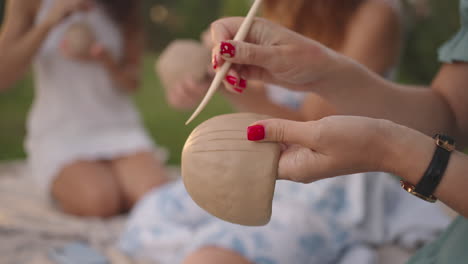 a group of young women are concentrating on applying patterns to clay products with the help of tools in a meadow in nature in an open space. women's hands decorate the product in close-up.