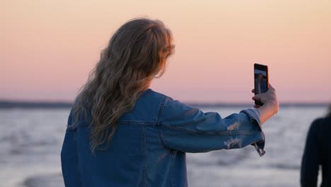 shot from side how young beautiful woman takes a selfie near the sea