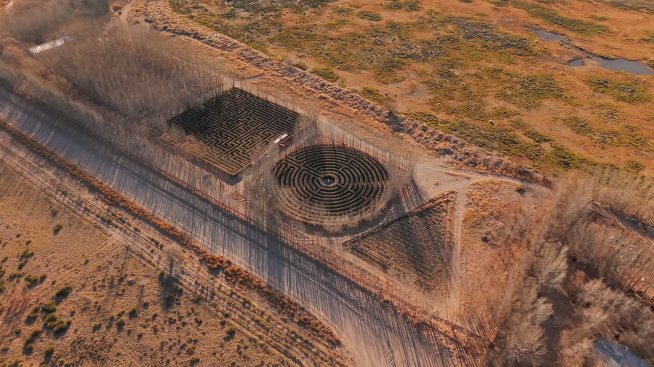 Labirinti di siepi circolari, quadrati e triangolari a Malargüe, Mendoza, circondati da alberi spogli nella luce del tardo autunno. Veduta aerea dall'alto inclinata verso il basso