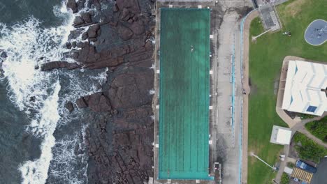 large waves crash close to a coastal community swimming pool while people exercise