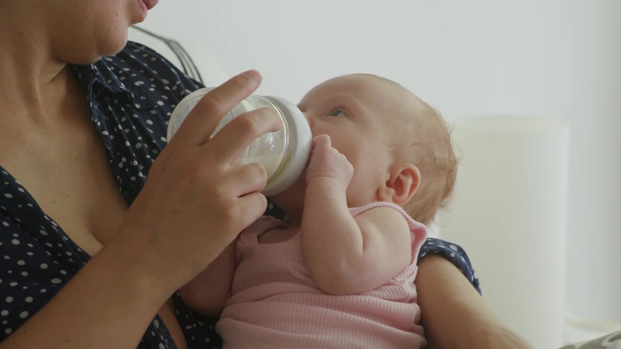 Bebé de ocho semanas bebiendo un biberón de leche en los cálidos brazos de su madre