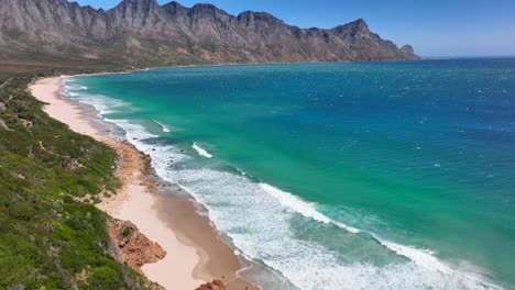 koeel bay dappat se gat drone aéreo cinematográfico olas de surf de viento que se estrellan impresionante playa de kogel bay costa de cape town sudáfrica costa acuática aguas azules profundas bahía de gordon jardín ruta hacia adelante pan up movimiento