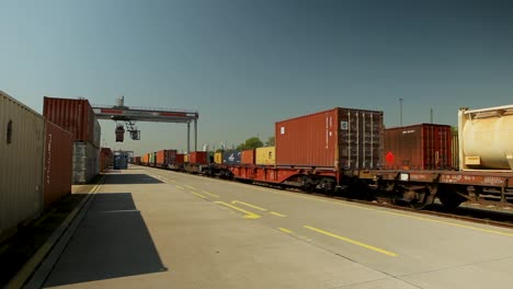 Tren-De-Carga-Con-Contenedores-Coloridos-En-Un-Muelle-Comercial-Durante-El-Día,-Cielo-Azul-Claro