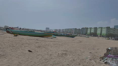 4k sweeping view of marina beach in chennai, india with traditional fishing boats and apartments in the background