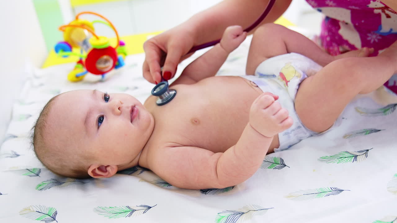 Doctor's hand puts stethoscope on baby boy's chest. Calm beautiful kid lying peacefully on the pediatrician's table. Close up.