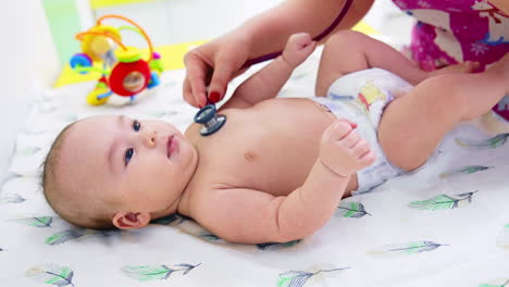 doctor's hand puts stethoscope on baby boy's chest. calm beautiful kid lying peacefully on the pediatrician's table. close up.