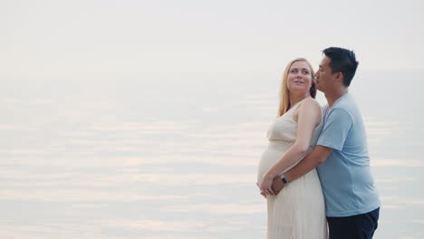 a young asian man hugs his pregnant wife on a sunset background over the sea multi-ethnic couples in