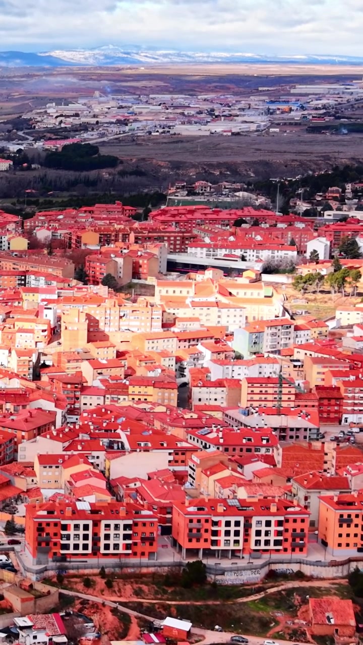 Stadtbild von Teruel, Spanien, mit Wohnblöcken mit orangefarbenen Dächern und bergigem Gelände in der Ferne, von oben betrachtet bei Tageslicht und bewölktem Wetter. Vertikales Video