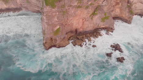 Cinematic-smooth-aerial-drone-shot-of-large-waves-crashing-into-huge-cliff-edge-in-uuwatu,-Bali-during-golden-hour-on-summer-sunset-3