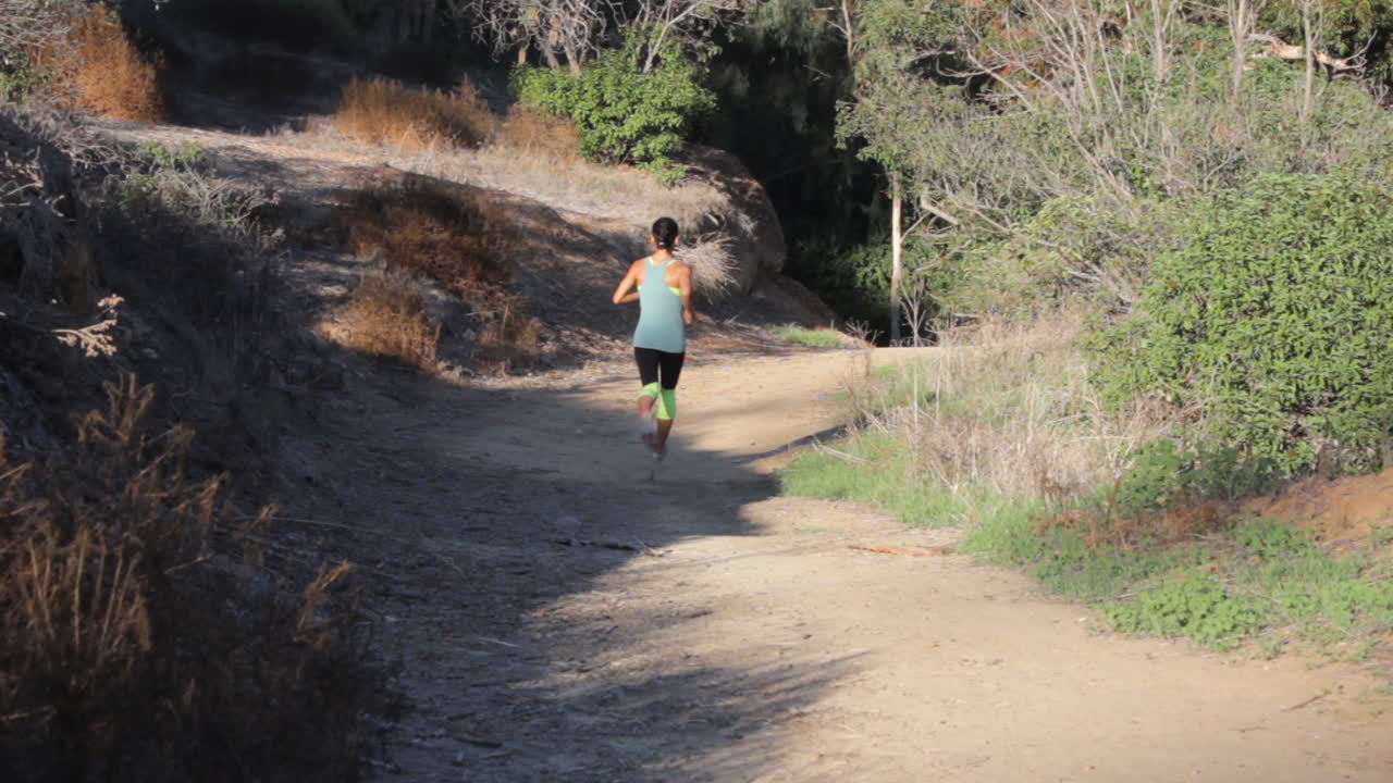 una hermosa corredora camina sin esfuerzo por un camino de tierra natural usando medias y un sostén para trotar