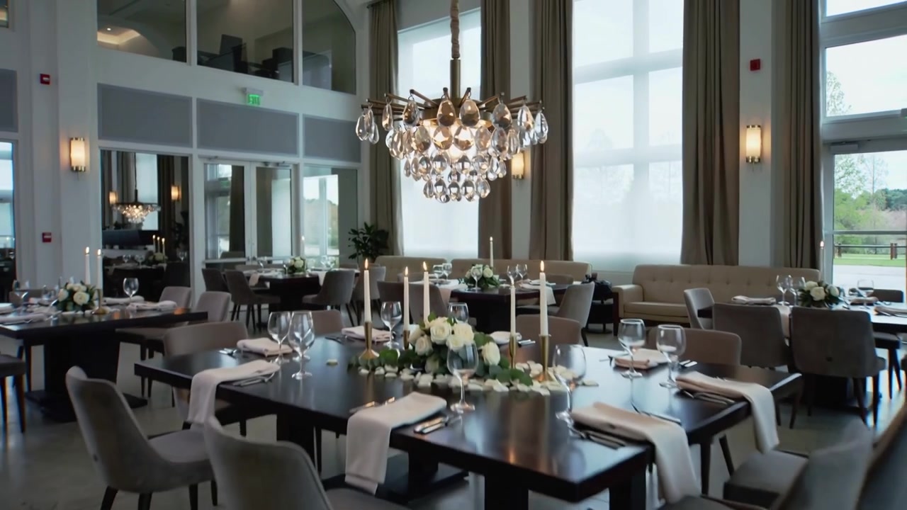 Cámara alejándose mostrando una lámpara de araña de cristal sobre mesas de comedor en una sala de eventos, con velas encendidas