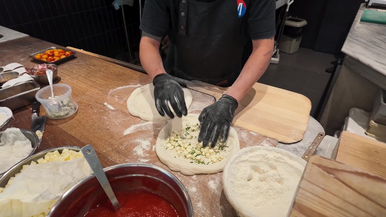 Chef che prepara impasto per pizza con formaggio e salsa di pomodoro nella cucina di un ristorante