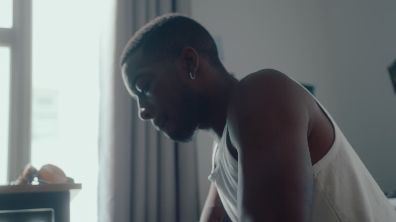 Young Black Man Sitting in Bedroom Dribbling a Basketball