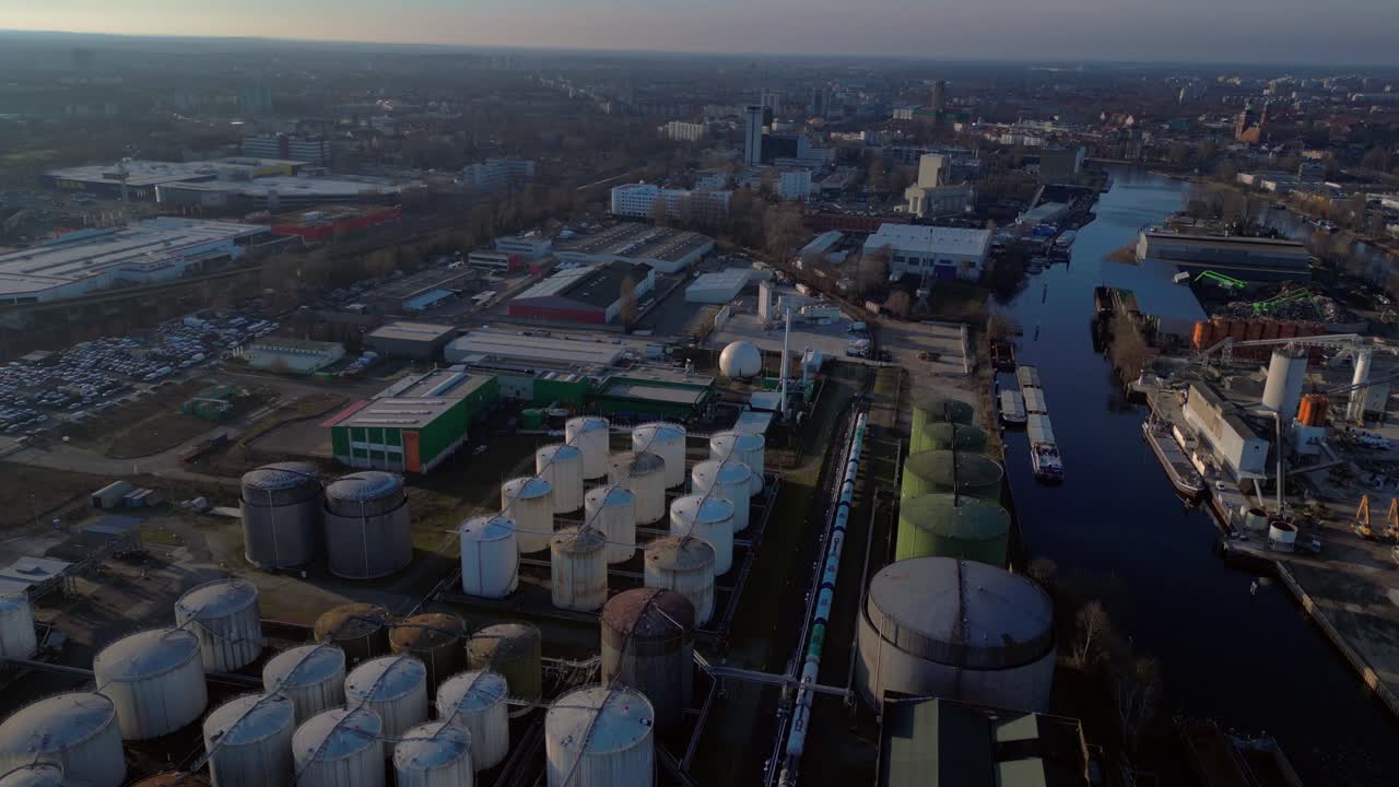 Berlin biogas plant with its large white tanks reflecting on the river next to it during sunset. Marvelous aerial view flight descending drone
