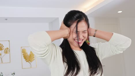 a woman covers her ears in a well-lit room, showing frustration or stress. neutral tones and modern decor enhance the scene