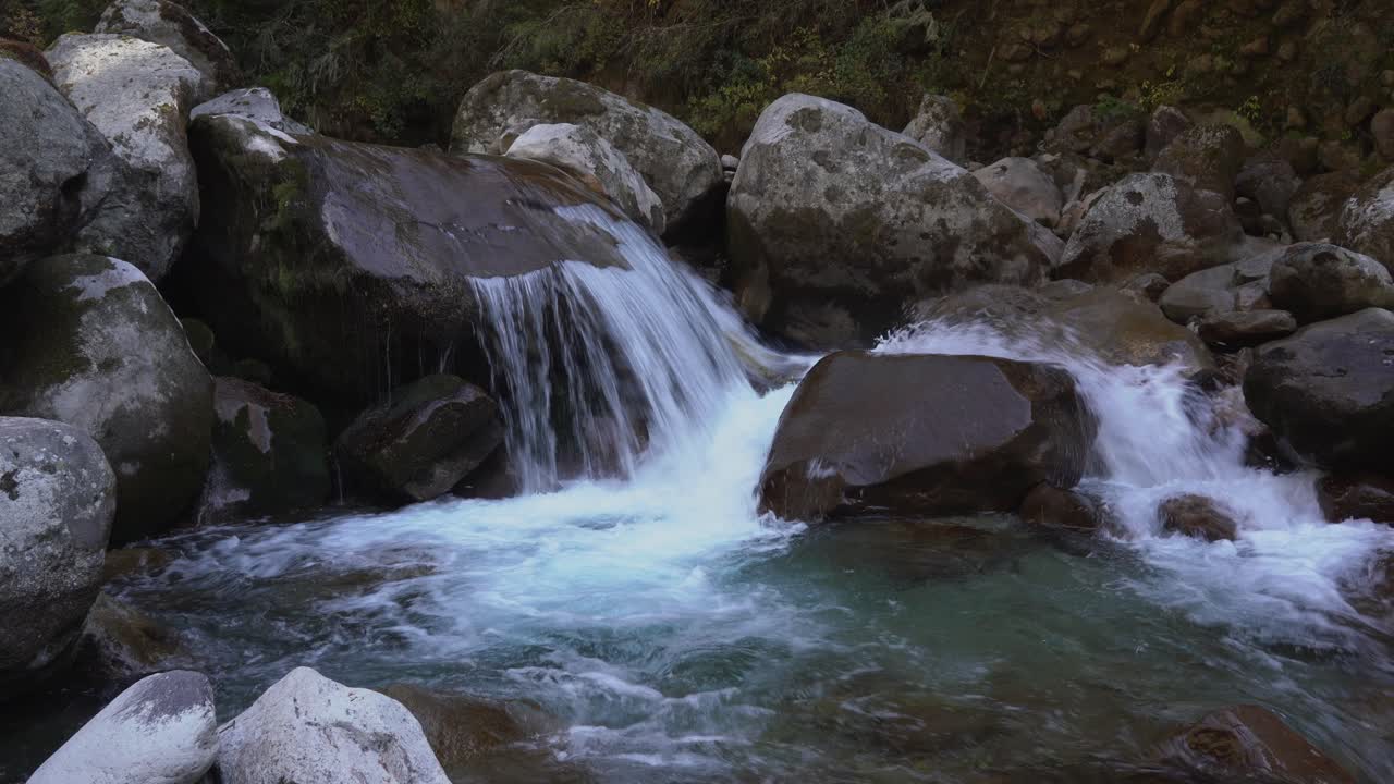 un pequeño arroyo que cae sobre las rocas haciendo una pequeña cascada en las montañas