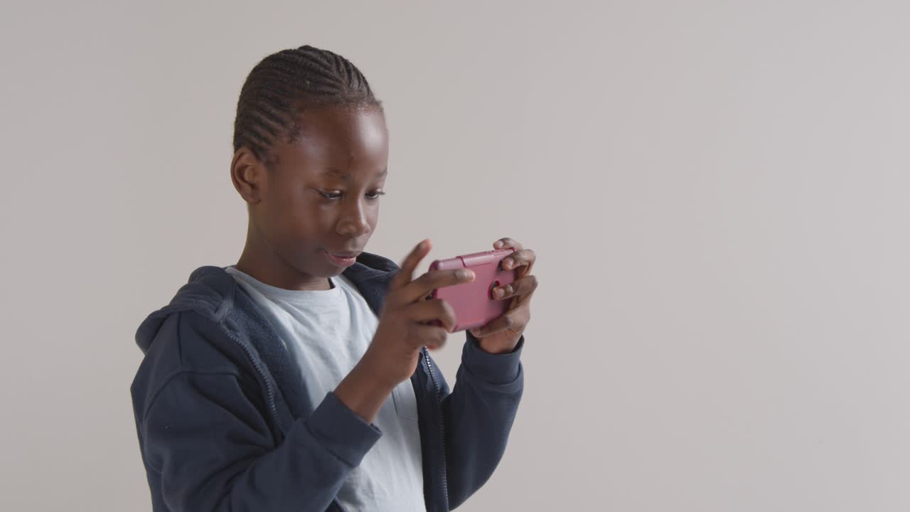 Studio Portrait Of Excited Boy On ASD Spectrum Gaming On Mobile Phone Against White Background