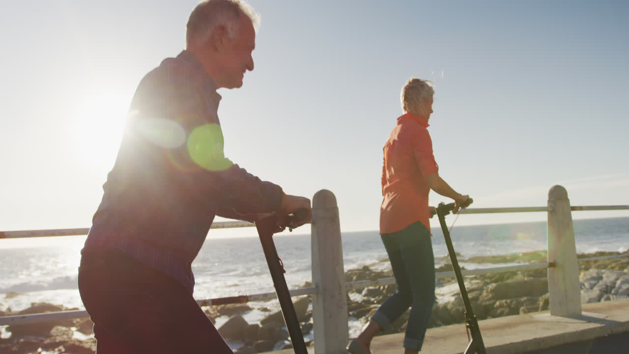 pareja de ancianos usando scooters electrónicos a lo largo de la playa