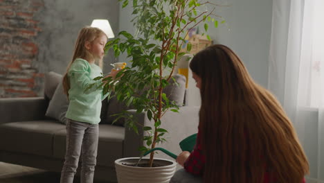 mother waters ficus with little daughter spraying leaves