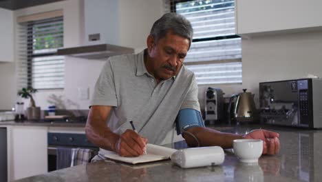 Senior-mixed-race-man-taking-blood-pressure-in-kitchen