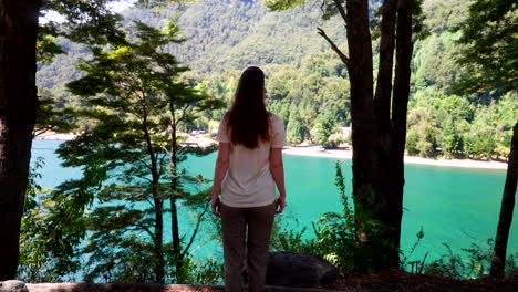 rear slomo tracking shot of female traveler under trees walking up to blue lake