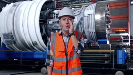 asian male engineer with safety helmet yelling with hand over mouth while standing with airplane engine maintenance conducted, analytics checking the turbine