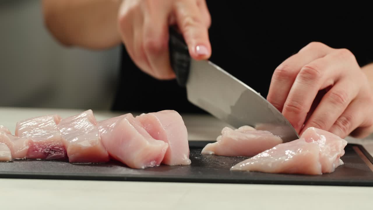 Man slicing raw turkey or chicken meat fillet on oak cutting board closeup, cooking with knife on restaurant kitchen. High quality 4k footage