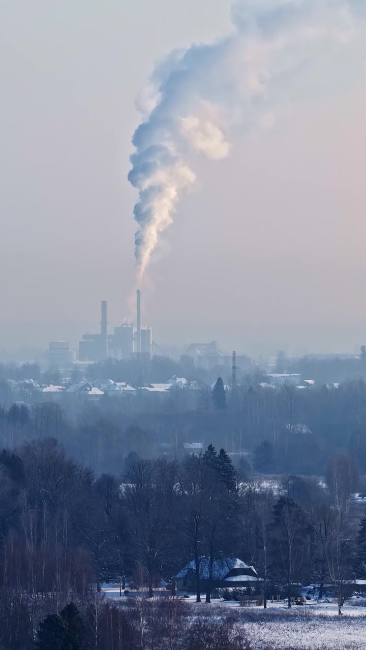 Factory chimney expelling a large plume of smoke into the atmosphere over a snowy rural village