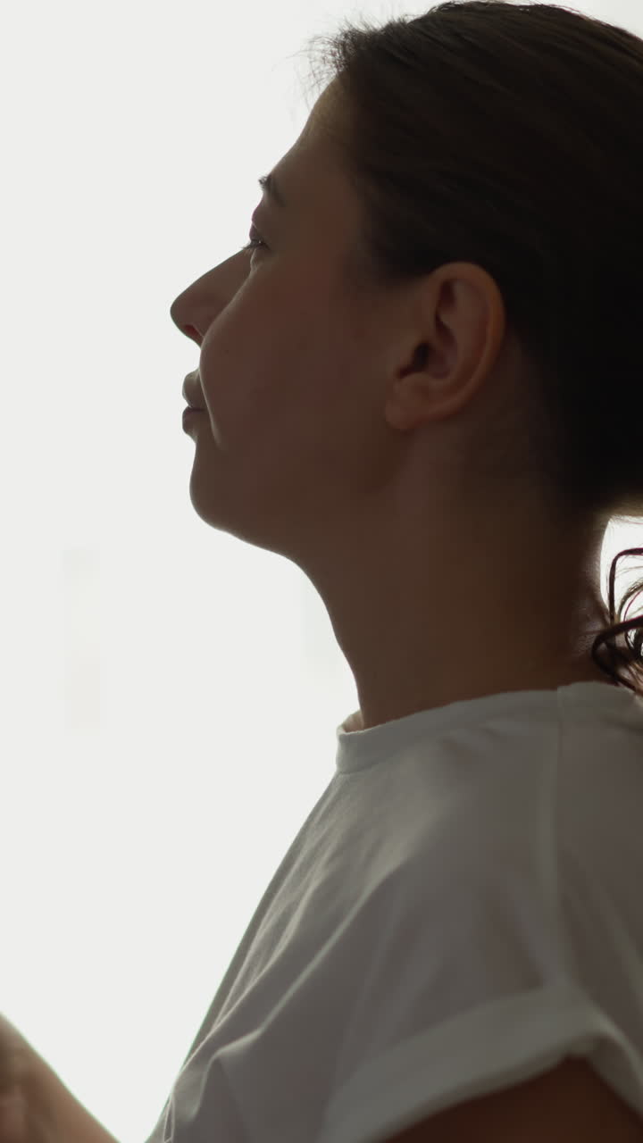 mujer bebe agua clara de pie junto a la ventana. dama bonita disfruta refrescante líquido frío de vidrio en casa cámara lenta. rutina saludable de la mañana