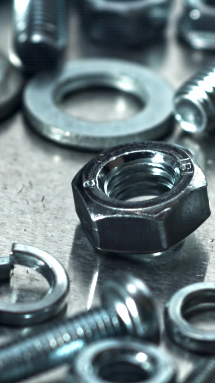 Dado metallico in rotazione su una superficie metallica con altri elementi di fissaggio