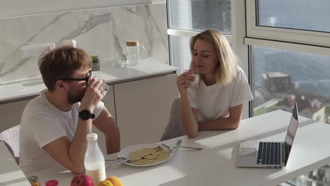 high angle view of couple smiling with joy at good morning in modern kitchen, affectionate young married couple drinking milk, having breakfast together in their apartment kitchen