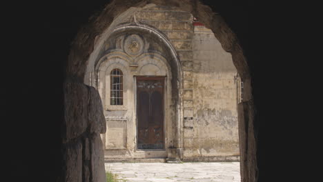 Darkened-stone-archway-leading-to-closed-door-in-monastery-courtyard