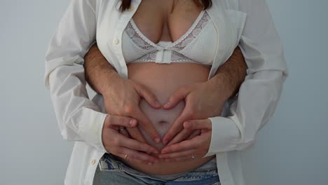 man embracing his pregnant wife with his hands in the shape of a heart