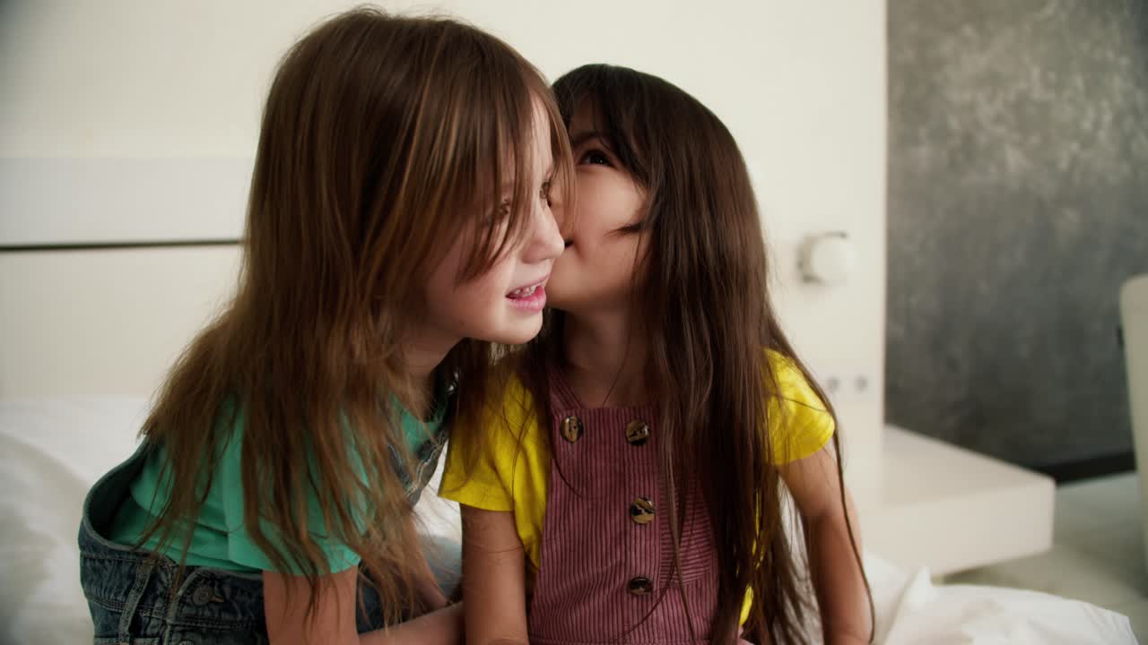 Lovely little cute girl combing the hair of her older sister, having fun and whispering gossips for fun