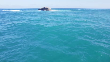 Expansive-view-of-calm,-turquoise-ocean-waters-with-a-distant-rocky-outcrop