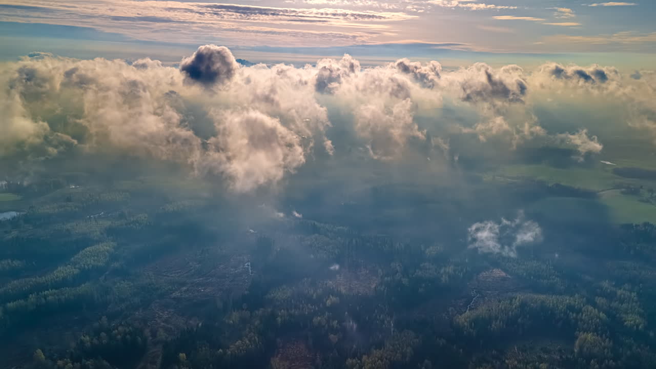 Layered clouds blowing in the hazy atmosphere above a the forest landscape - aerial timelapse