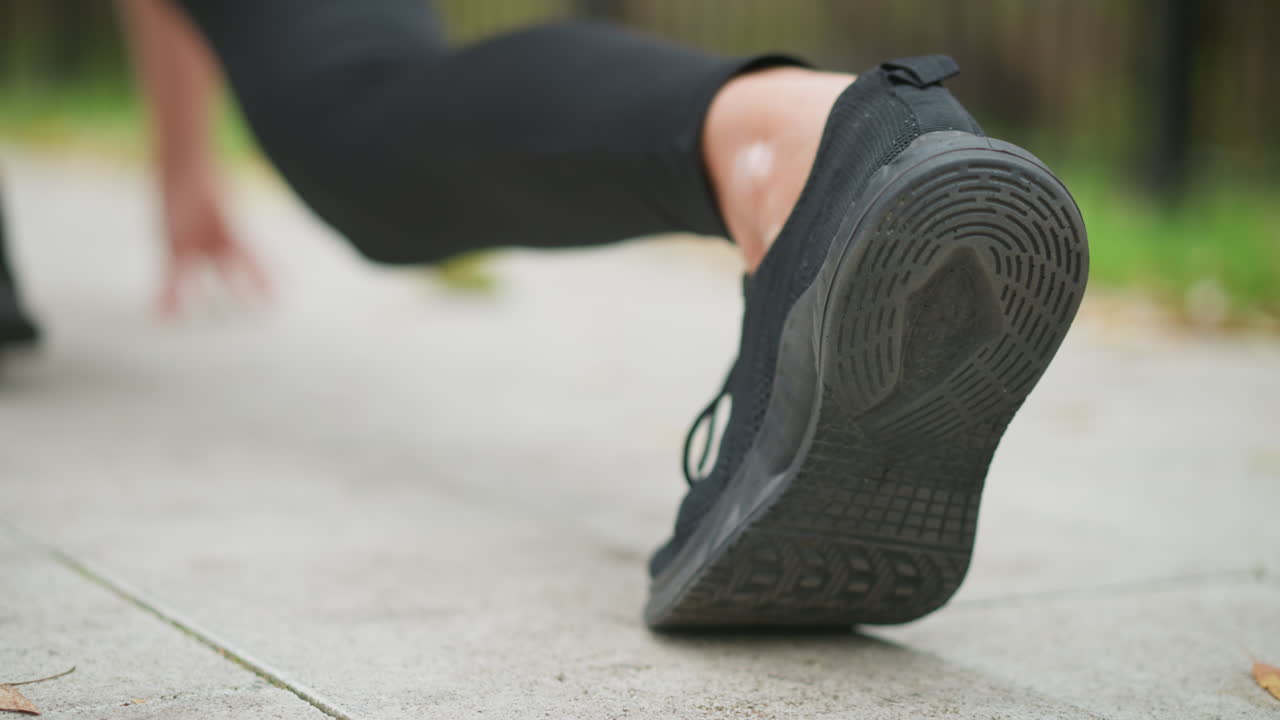Close-up view of runner's foot in black sneakers during a workout or jogging session on a smooth paved path, with blurred natural background, emphasizing movement and athletic footwear