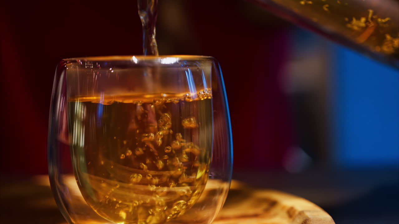Close up of a woman pouring tea from a French press into a double glass cup at a restaurant
