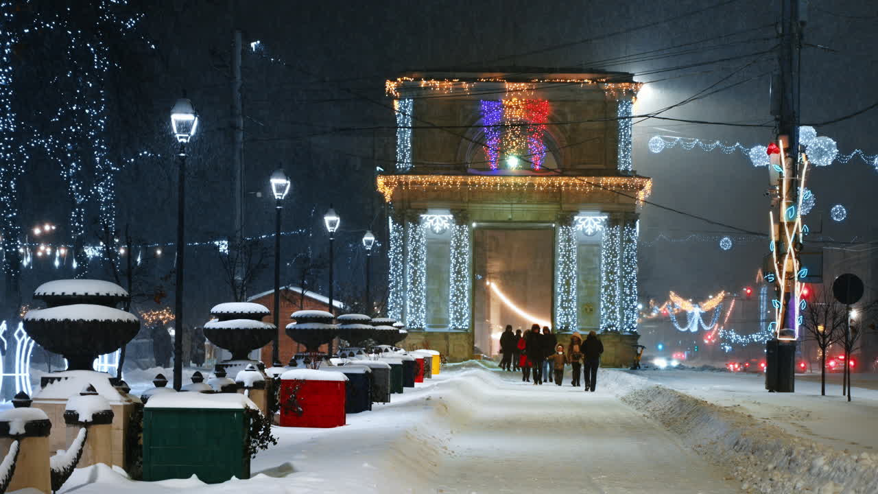 People walking on Great National Assembly Square during snowfall in the evening. The Triumphal Arch in background. Christmas decorations
