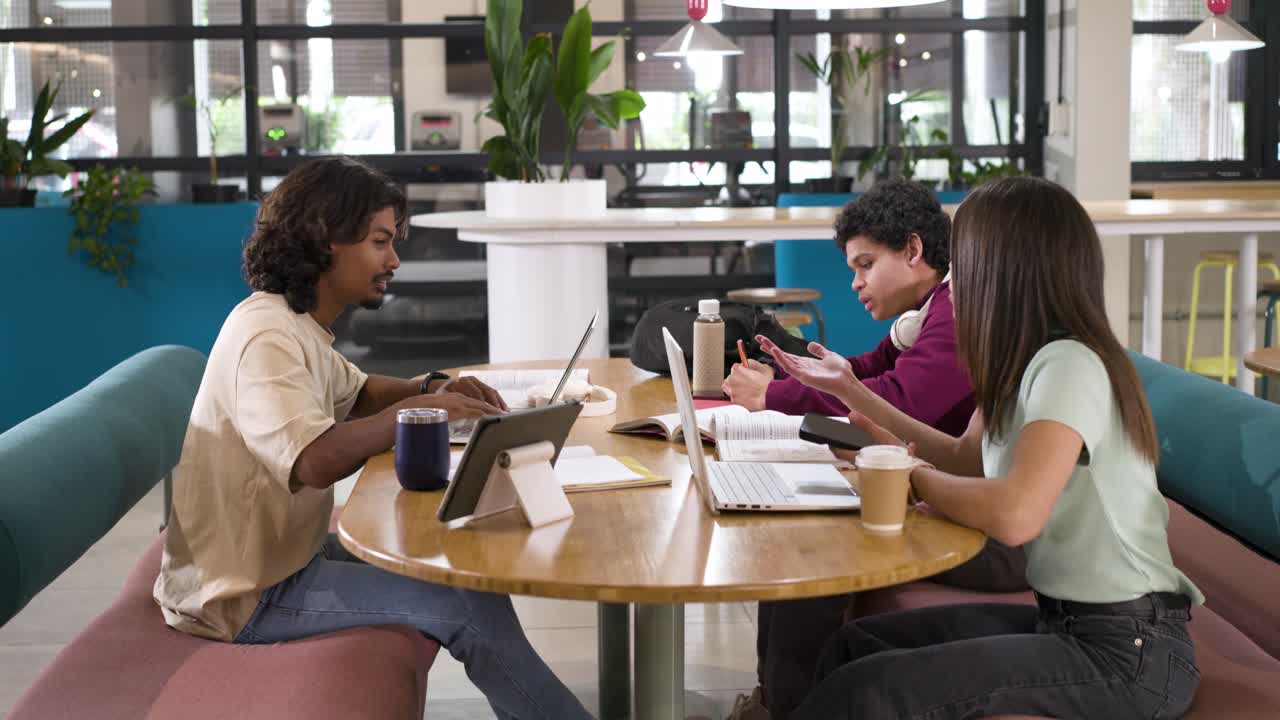 Diverse coworkers following left member gesturing collaborating on laptops at shared workspace